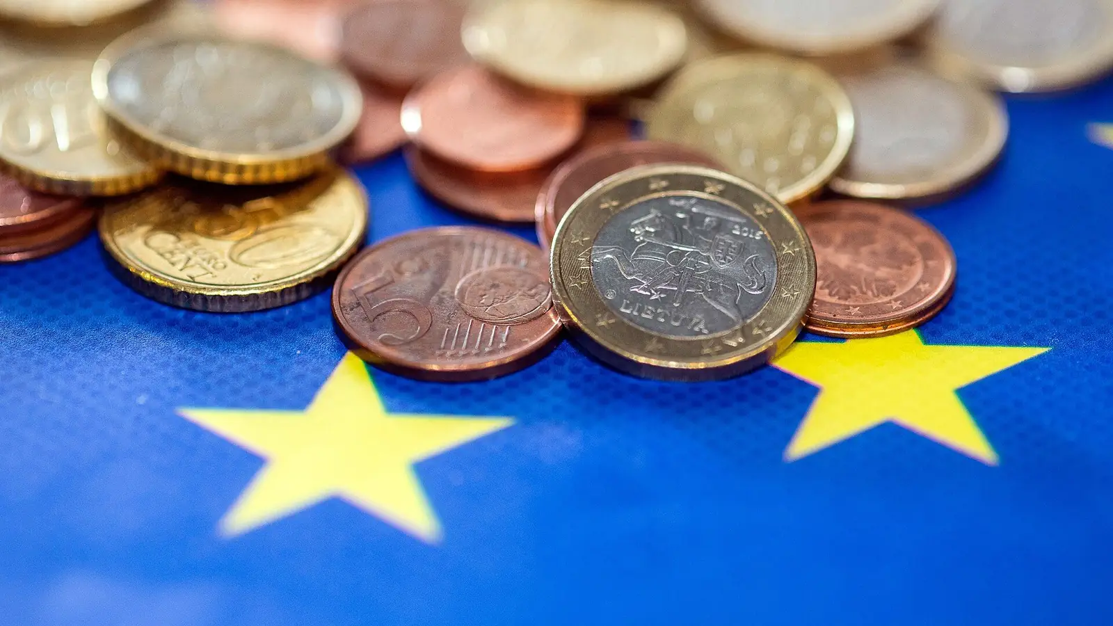 Monedas de euro sobre la bandera de la Unión Europea